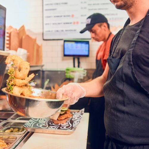 A man wearing gloves and an apron tosses fried shrimp with seasonings