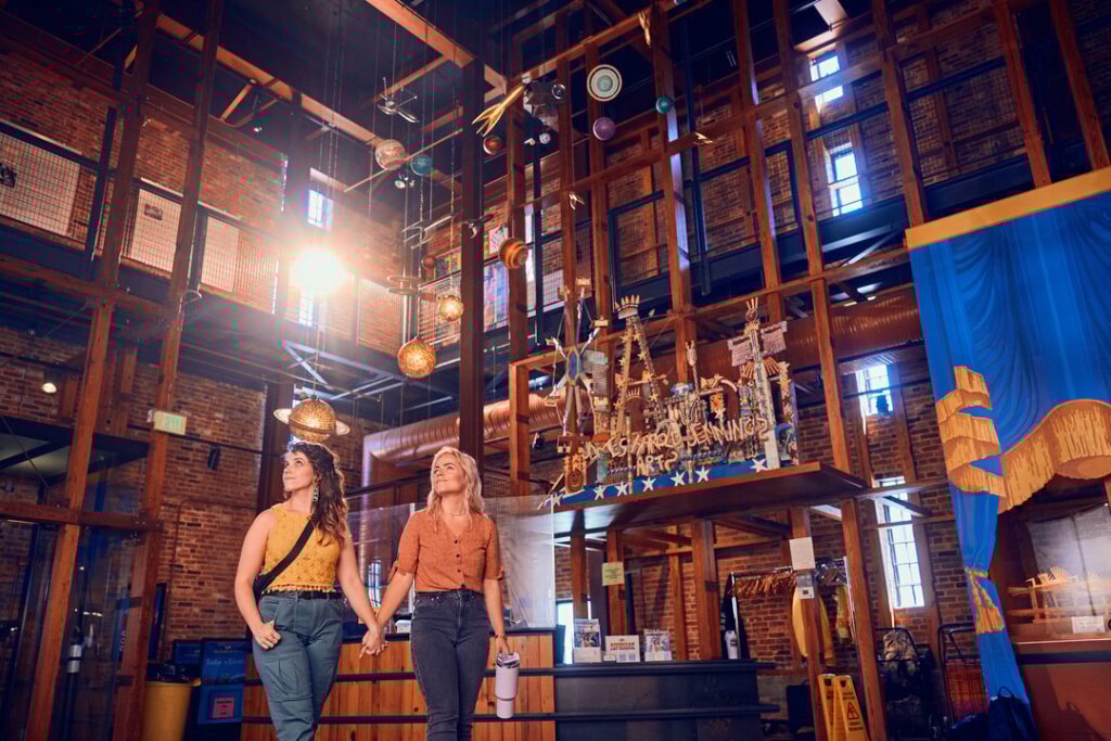 A female couple holds hands and walks through an industrial warehosue