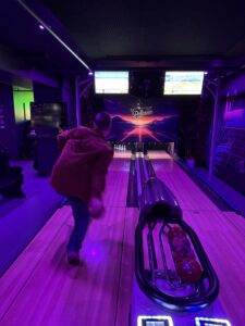 A man bowls in a room lit with purple lights