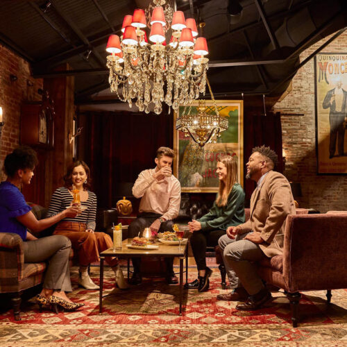 Five customers enjoy drinks on couches and chairs underneath a chandelier at the Elk Room in Baltimore.
