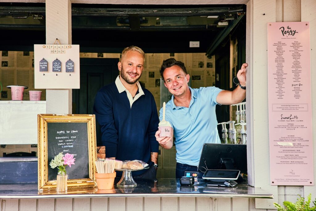 Two men smile behind a snowball stand