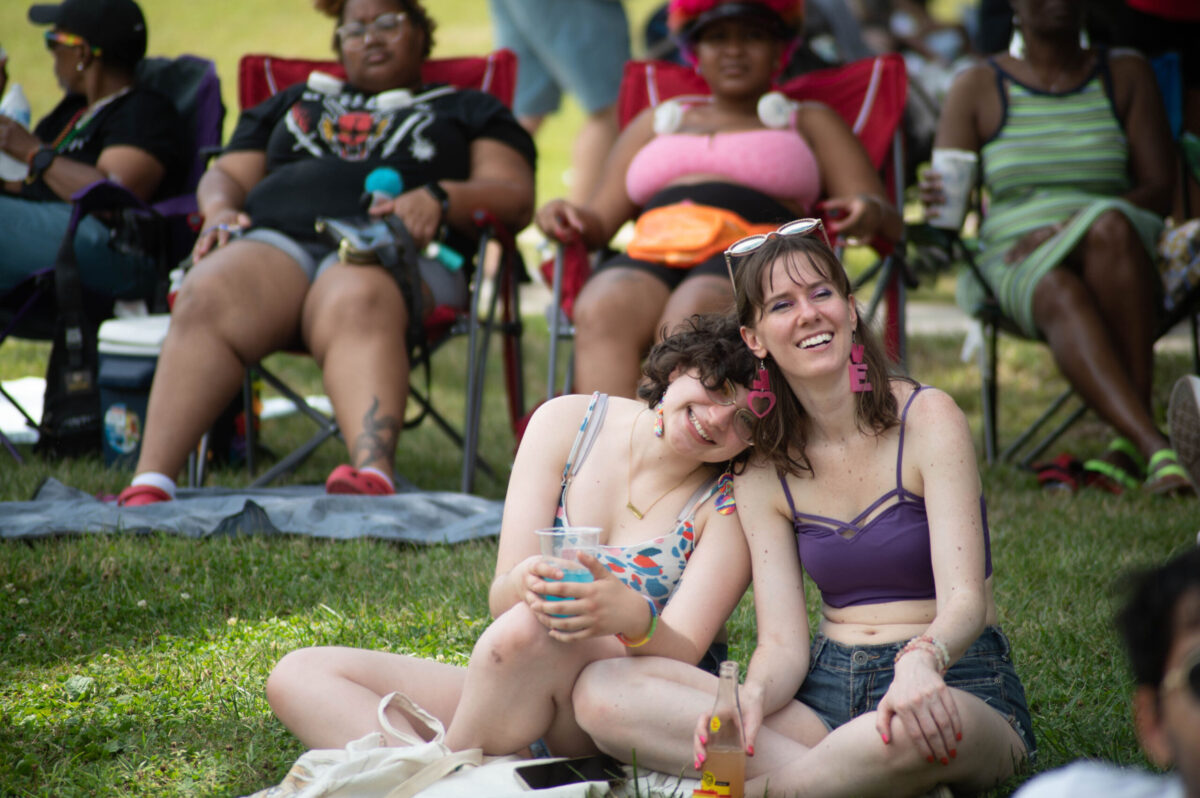 The white women lean into each other while sitting on a lawn