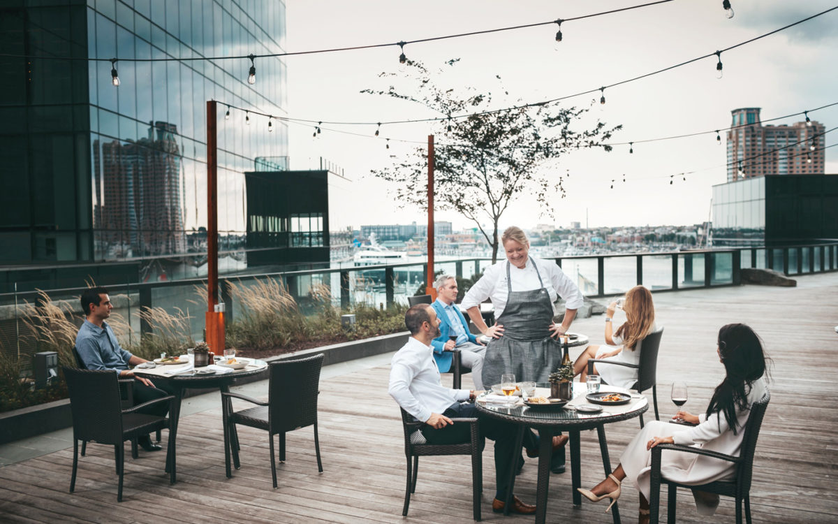 Diners sitting at tables on the boardwalk by the water on a cloudy day.
