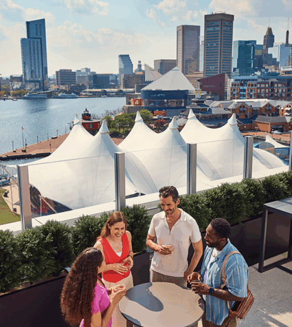 Two men and two women talk over drinks on an outdoor deck with a view of Pier 6 Pavilion